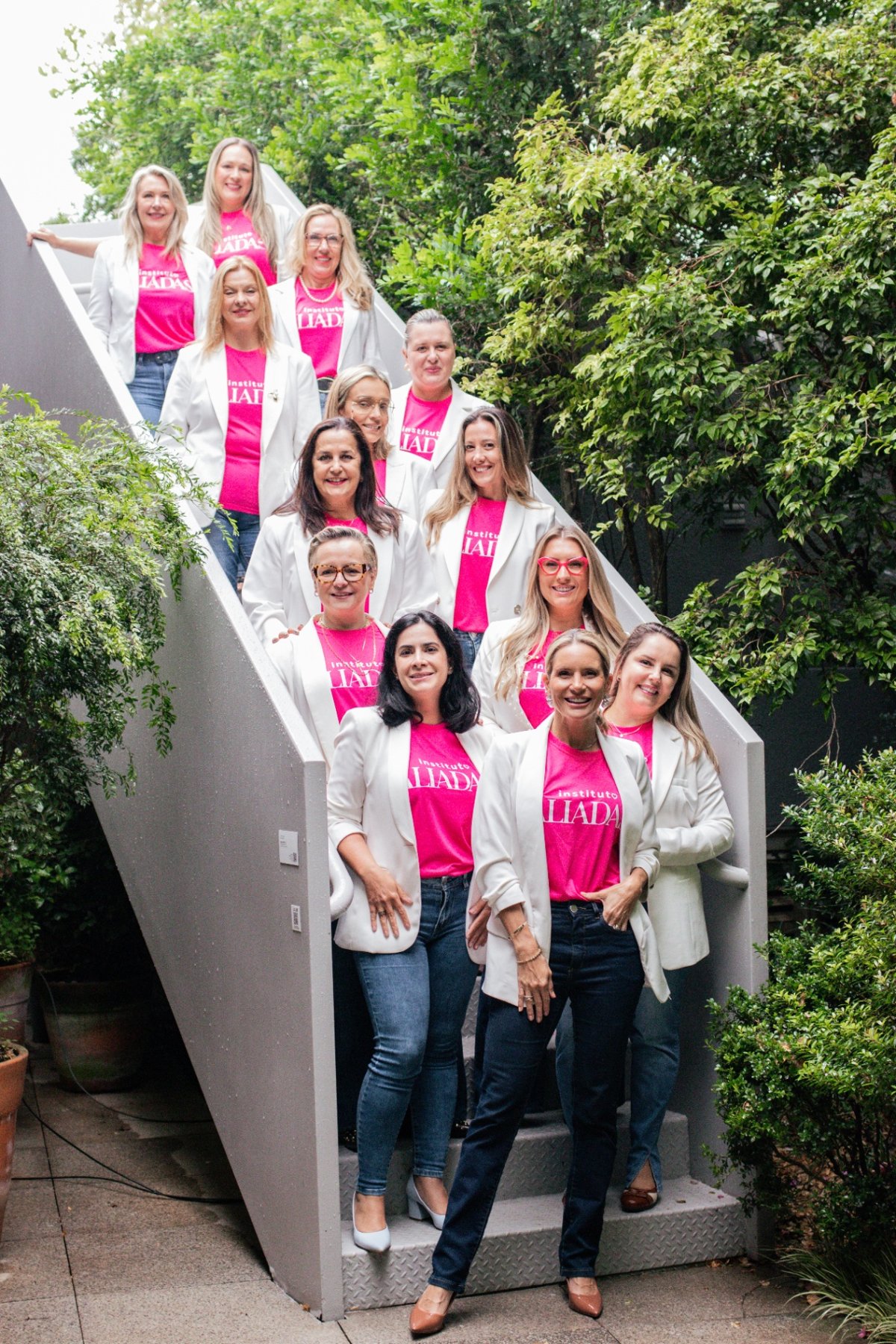 Equipe do Instituto Aliadas reunida em escadaria, com camisetas rosa do instituto